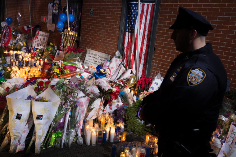 Image: An NYPD police officer stands guard beside a makeshift memorial