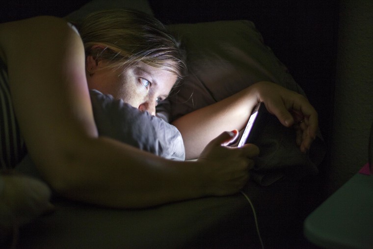Photo: A woman checks her cellphone in bed.
