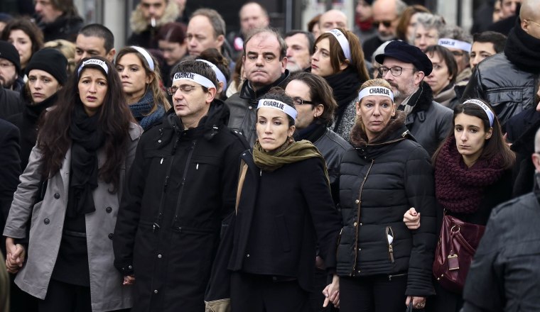 Image: Cartoonist Corinne Rey (3rd left in green scarf) known as Coco, a survivor of the attack on the Charlie Hebdo satirical magazine, and other staff members, link arms as the take part in a Unity rally "Marche Republicaine" on January 11, 2015 in Pari
