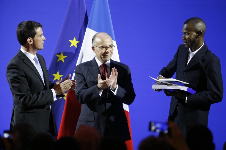 Image: French Prime Minister Valls and Interior Minister Cazeneuve applaud as Lassana Bathily, 24, holds his citizenship papers during a ceremony at the Interior Ministry in Paris