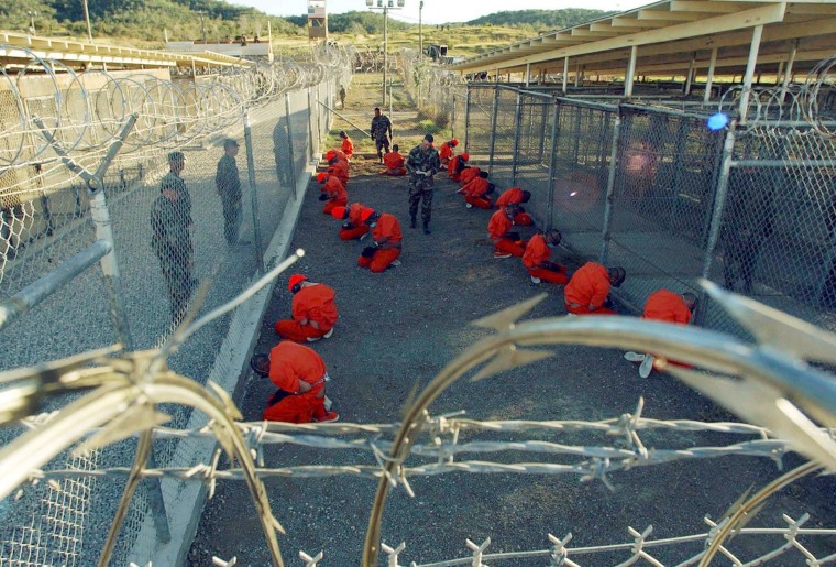 Image: Detainees in orange jumpsuits sit in a holding area at Naval Base Guantanamo Bay