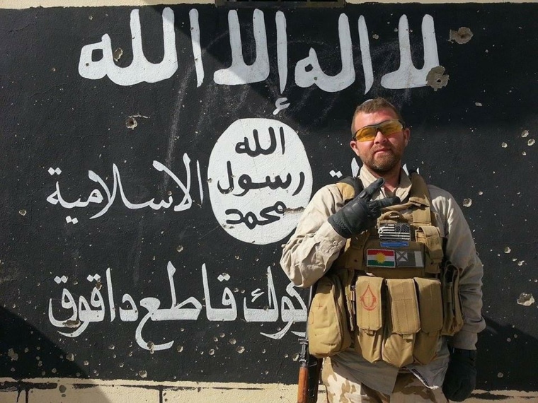 American Jeremy Woodward poses in front of an ISIS emblem painted on a wall in northern Iraq where he's joined Kurdish troops in their fight against ISIS.