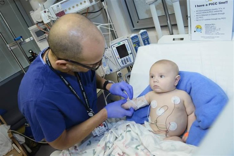 Dr. Darryl Miles carefully adjusts a new mesh bandage around the spot where a central line was inserted into the arm of 3-month-old Riley Moss, a patient in the PICU.