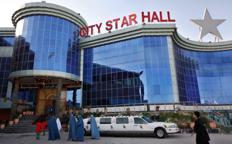 Image: Afghan women covered in burqas walk pass a parked limousine out side a wedding reception hall in Kabul