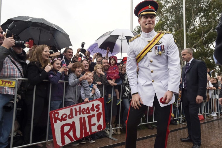 Prince Harry reacts after shaking hands with kids holding up a sign reading 'Red Heads Rule' during a visit to the Australian War Memorial in Canberra