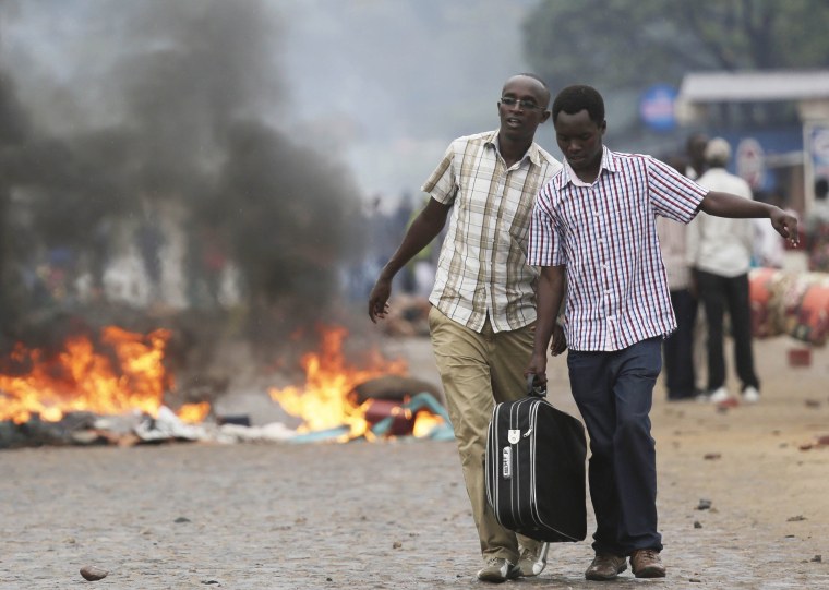 Two men carry a suitcase past a burning barricade in Bujumbura, Burundi Thursday, April 30, after the government issued and ordered for all university campuses to close down.
