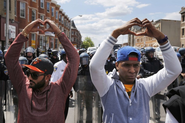 Image: Members of the community make heart gestures with their hands in front of a line of police officers in riot gear, near a recently looted and burned CVS store in Baltimore