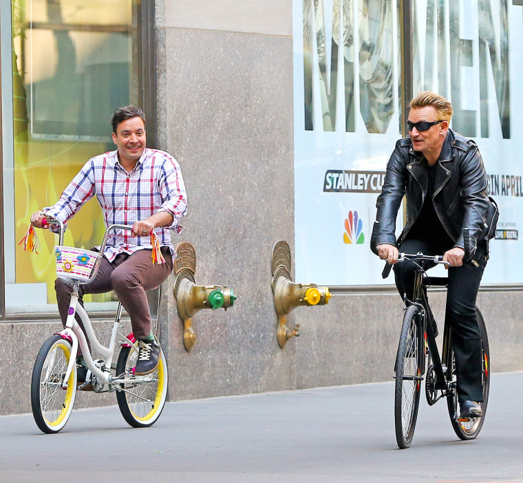 Bono and Jimmy Fallon seen riding their bikes on sidewalk while filming a set for 'The Tonight Show Starring Jimmy Fallon' in New York City