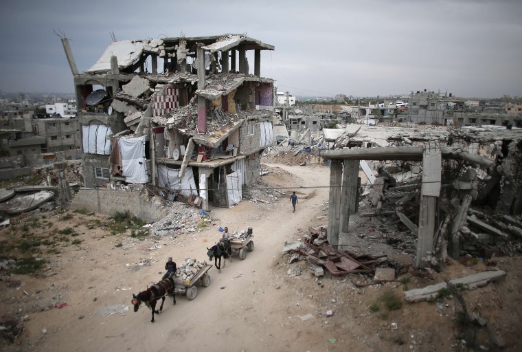 Image: Palestinians ride their donkey-carts in the middle of rubble and destroyed buildings