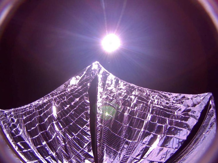 A picture transmitted from the LightSail solar sail spacecraft in orbit shows its reflective sails partially deployed, with the sun glaring in the background.