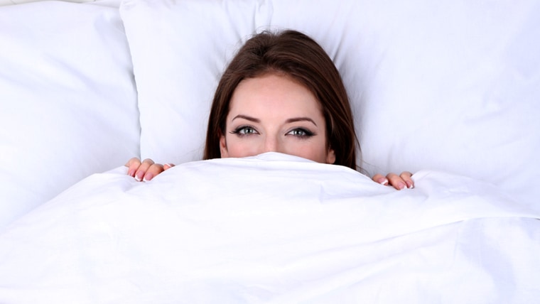 woman looks out under covers in bed