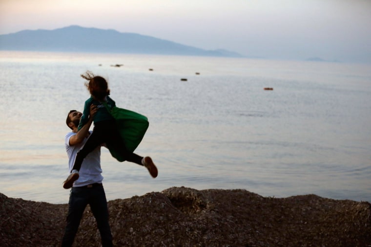 Image: A Syrian migrant holds up his daughter as lifejackets float on the water after their arrival from the Turkish coast