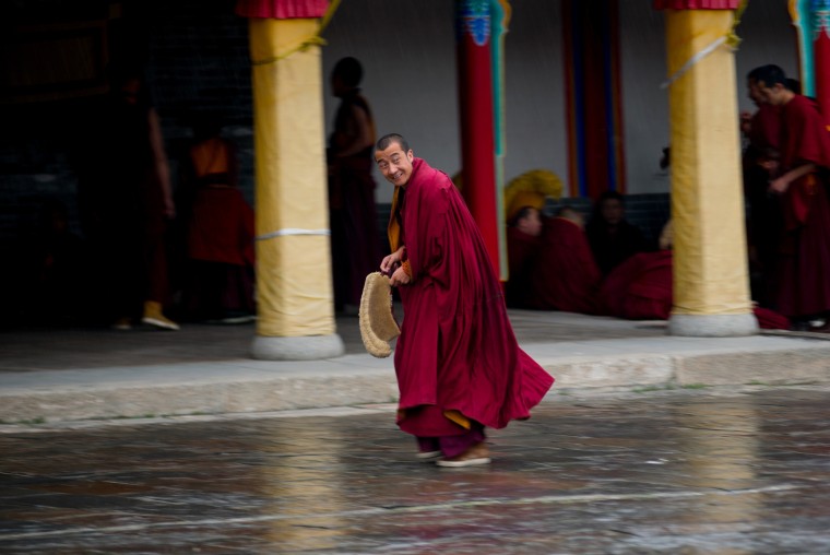 Image: A lama smiles as his prepares to leave the monastic debate ground to take shelter from the rain