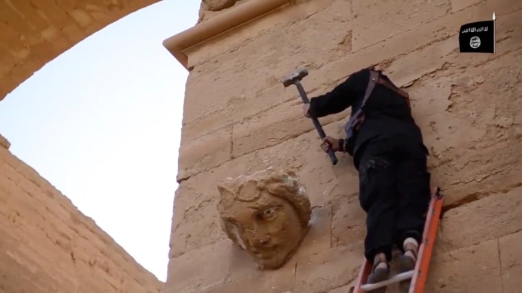 Image: A militant hammers away at a face on a wall in Hatra, Iraq