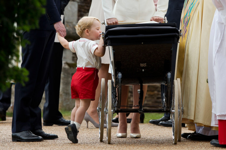 Image: Britain's Prince George gets up on tiptoes to peek into the pram of Princess Charlotte