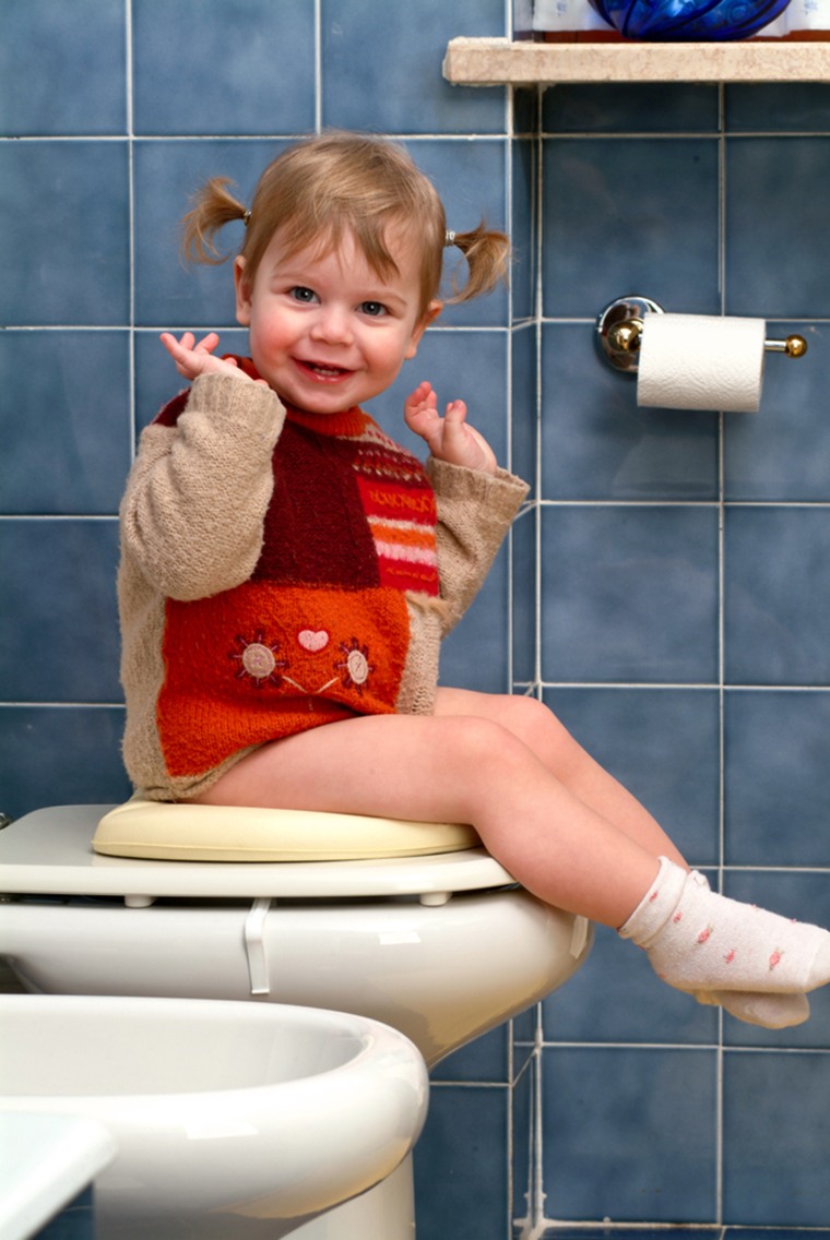 Toddler girl potty training holding toilet paper in bathroom Stock