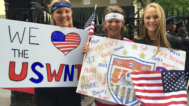 Fans stand on parade route with signs