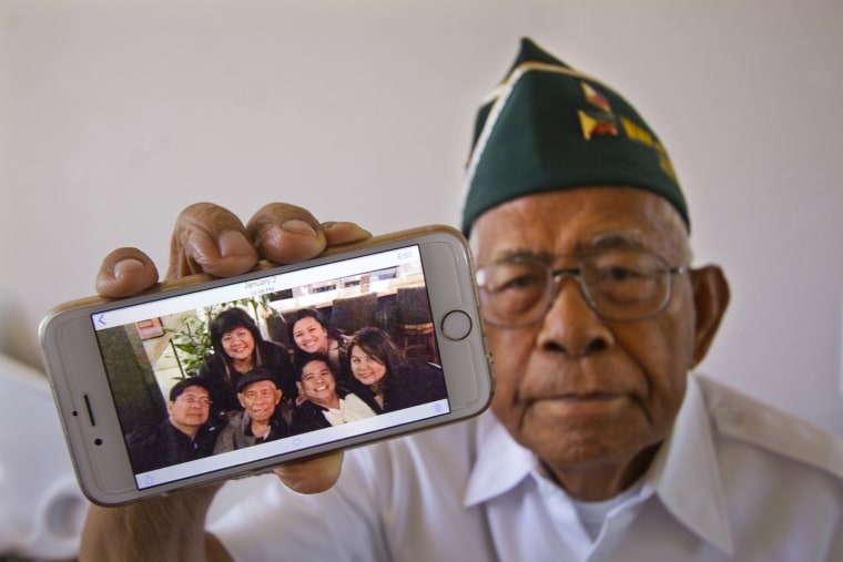 In this March 27, 2015 photo, Filipino World War II veteran Artemio Caleda holds up a family photo at his home in Ewa Beach, Hawaii. Although the shrapnel scar Caleda picked up picked up during World War II is now seven decades old and faint, it serves as a stinging reminder that Caleda is still fighting a battle: to have his three grown sons join him in the United States.