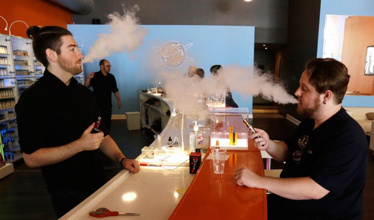 Image: Scot Taylor, left, manager of the Vapor Spot and customer Bruce Schillin, 32 exhale vapor from e-cigarettes