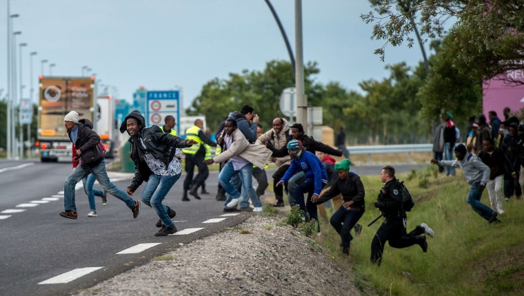 Image: Police officers try to prevent migrants from reaching the Channel Tunnel
