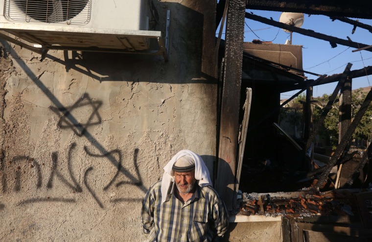 Image: A Palestinian man stands next to a graffiti reading in Hebrew "Revenge"