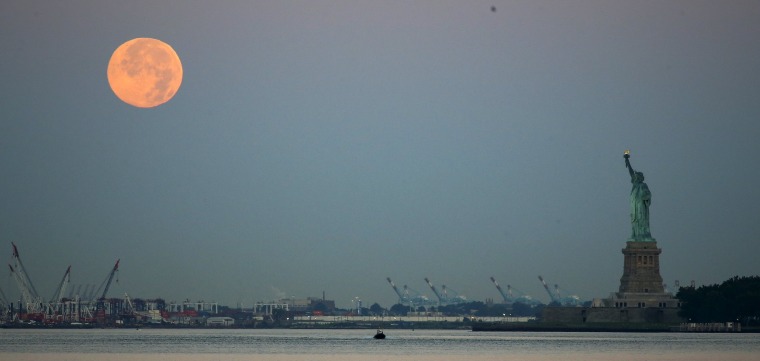 Image: A full moon, known as the Blue Moon, is seen over the Staten Island Ferry while it makes its way to New York