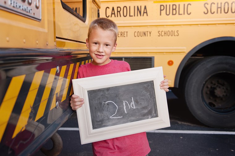 Boy holds second-grade sign near school buses
