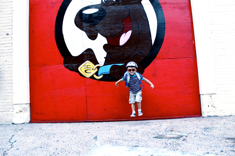 Boy takes back-to-school photo in front of a bright red wall