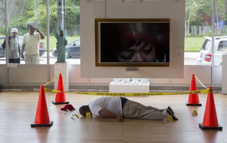 Image: Two men look through a window at an art installation depicting the body of Michael Brown, made by artist Ti-Rock Moore at Gallery Guichard in Chicago