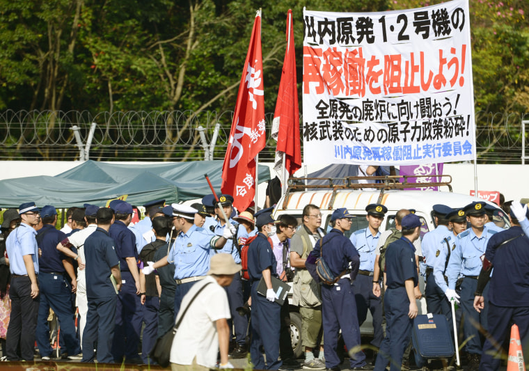 Image: Police officers stand guard as protesters stage a rally at the gate of the Sendai Nuclear Power Station