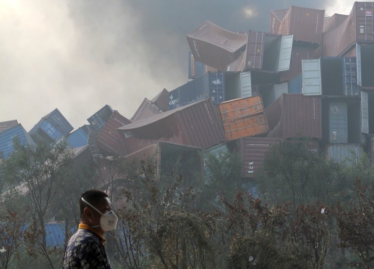 Image: A man wearing a mask walks past overturned shipping containers in Tianjin