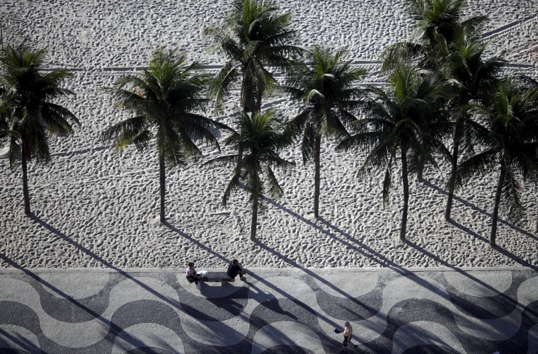 Image: People sit on a bench on the sidewalk at Copacabana Beach in Rio de Janeiro, Brazil