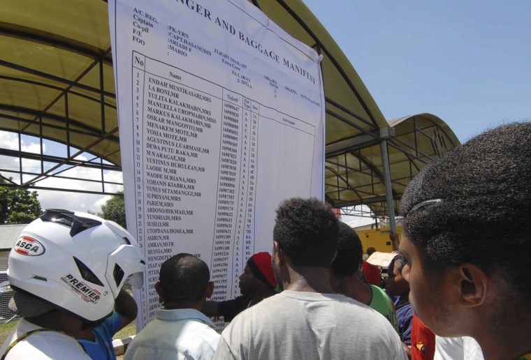 Image: People look at a passenger and baggage manifest of the crashed Trigana flight