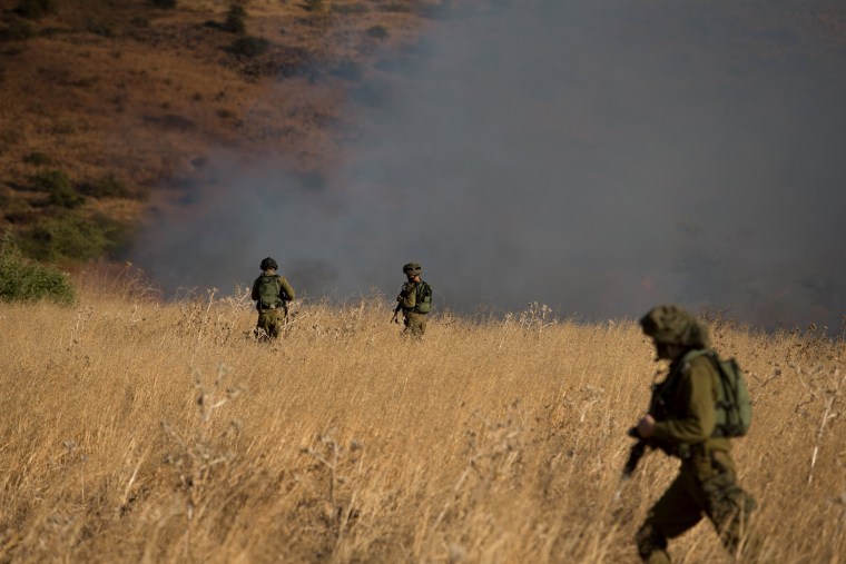 Image: Israeli soldiers patrol next to a smoke from a fire caused by a rocket attack in northern Israel, near the Lebanese border