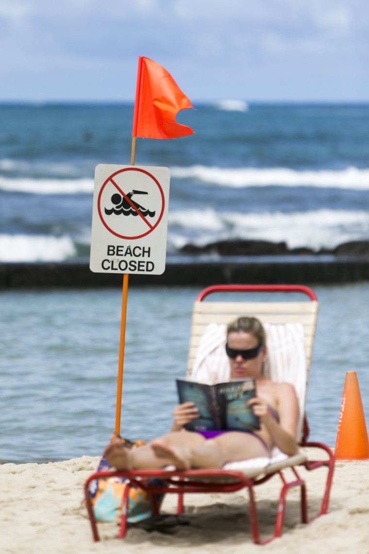 Image: A sunbather reads a book behind a beach closed sign at Waikiki Beach in Honolulu, Hawaii