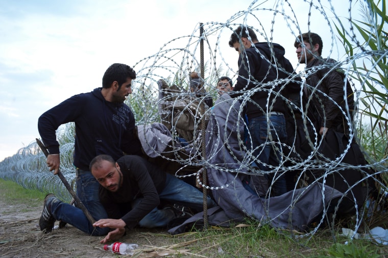 Image: Refugees cross into Hungary underneath the razor wire border fence on Wednesday.