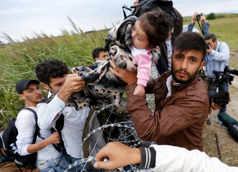 Image: A migrant hands a girl to another migrant over razor wire on the Hungarian-Serbian border fence, Wednesday.