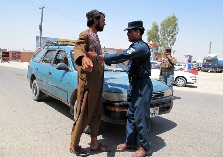Image: An Afghan security member frisks a man at a checkpoint on a roadside in Helmand