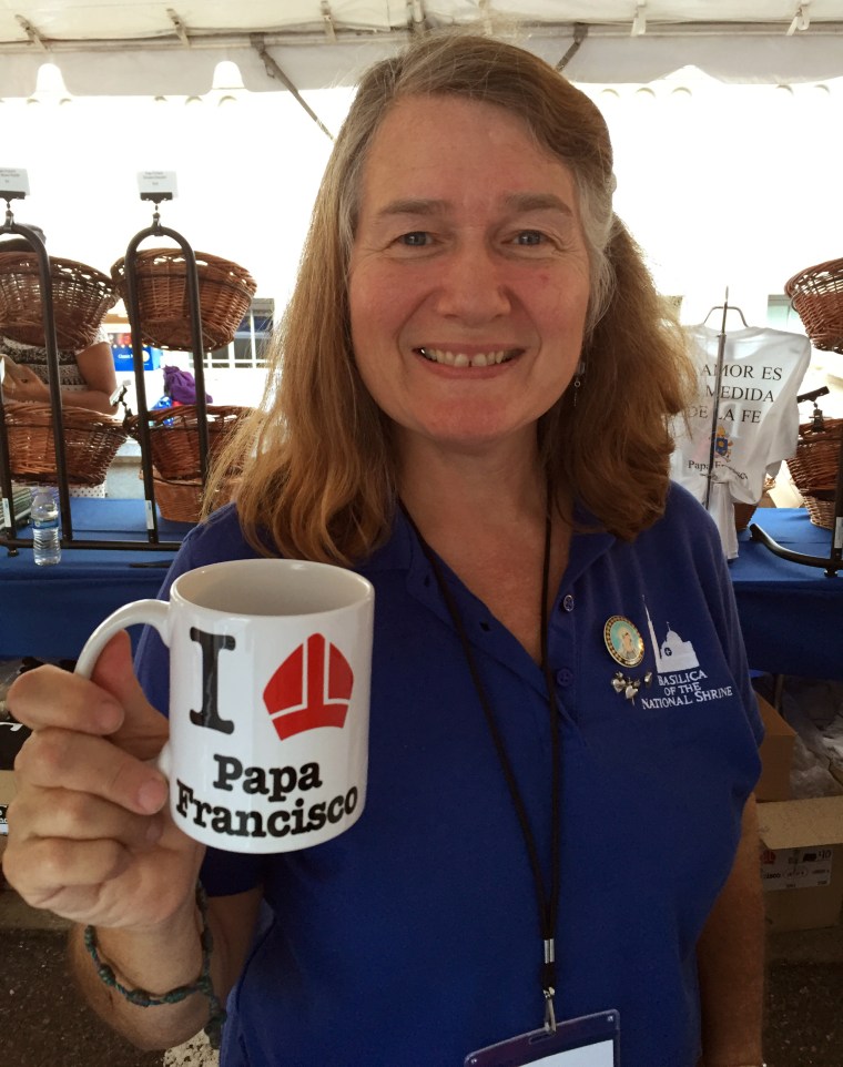 Cathy Bewley, staffing the gift shop at the Basilica of the National Shrine, holds up a $10 mug. There are now long lines to check out the merch.