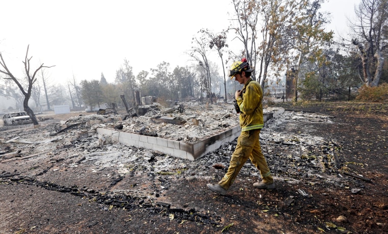 Image: A firefighter walks past the remains of a house destroyed in a wildfire