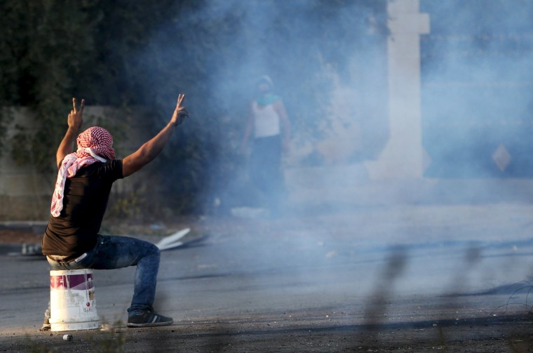 Image:  Palestinian protester sits on a bucket that he used to cover a tear gas canister fired by Israeli troops during clashes near the Jewish settlement of Beit El, near the West Bank city of Ramallah