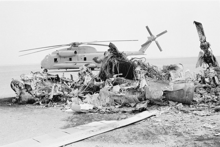 Image: Remains of a burned-out U.S. helicopter lies in front of abandoned chopper in the eastern desert region of Iran
