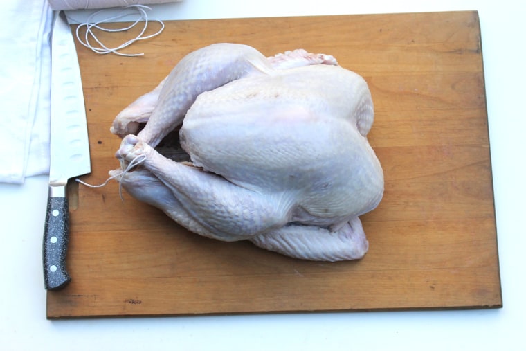 How to make bacon-wrapped turkey: place the turkey on a cutting board and tie the legs together