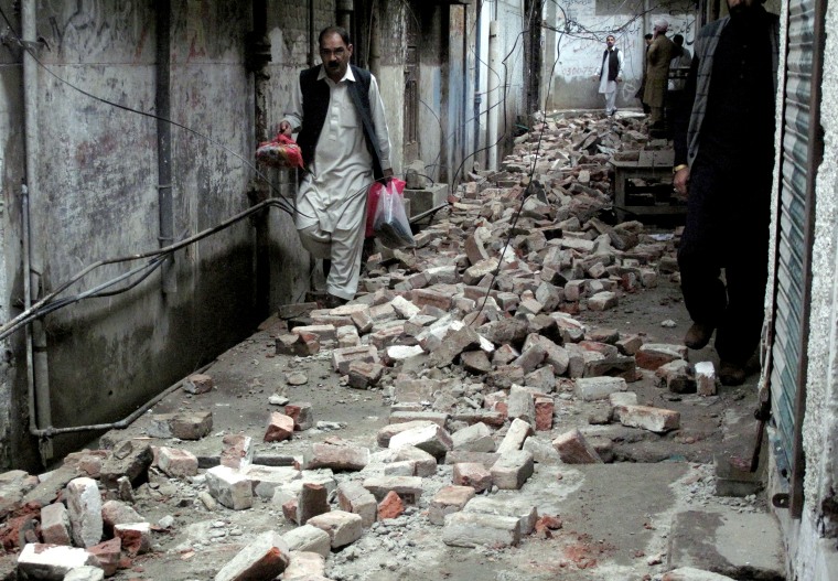 Image: A man with his belongings walks past the rubble of a house after it was damaged by an earthquake in Mingora