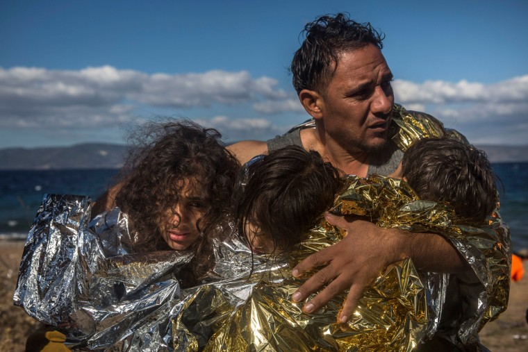 Image: A man holds three children wearing thermal blankets