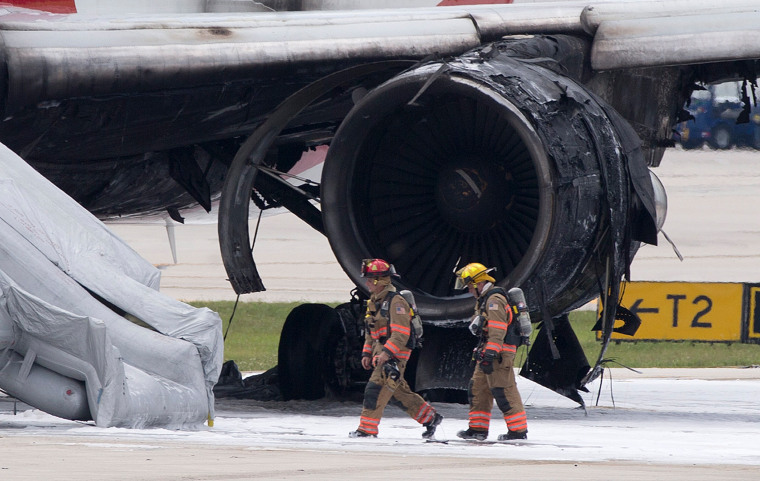 Image: Firefighters walk past a burned out engine