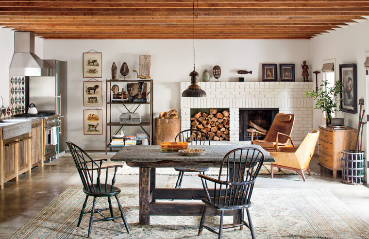 This was the first fully realized cabin. I mix and matched a set of early American Windsor chairs around a nineteenth-century stone-top table from Belgium. The kitchen has a custom bluestone counter and sink with stained oak cabinet. A vintage industrial shelving unit displays my collection of nineteenth-century African masks, taxonomy drawings, and American primitive artifacts. The vintage Moroccan rug in front of the fireplace feels fresh with Danish midcentury lounge chairs. The chest behind them is Gustavian. RIGHT: The custom sofa by Brenda Antin, Scimitar chair by Ib Kofod-Larsen, and contemporary bluestone coffee table made for a comfortable living room in this cabin. Books, along with a French artist’s model of a horse and a figurine, flank the chipped, stack stone fireplace. The rug is hemp, handwoven in Tibet.