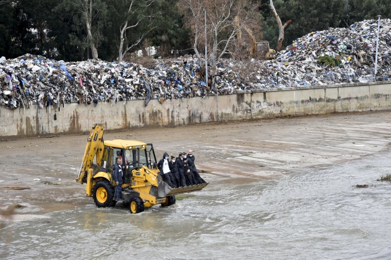Image: "You Stink" activists ride on the front of a loader during a campaign to remove piled garbage on the bank of Beirut river