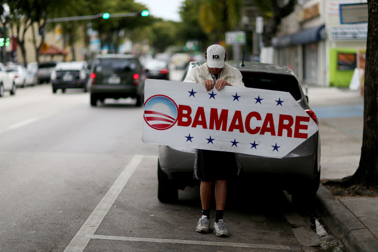 Image: Pedro Rojas holds a sign directing people to an insurance company where they can sign up for the Affordable Care Act