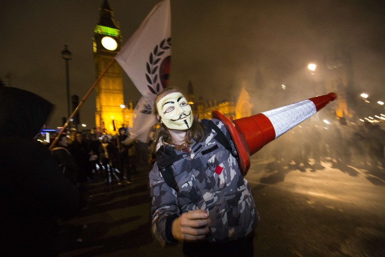Image: An anti-capitalist protester wearing a Guy Fawkes mask carries a traffic cone during the "Million Masks March"